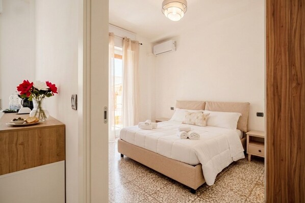 A bedroom with a bed, bedside tables, a nightstand, a wooden dresser, and a vase with flowers.