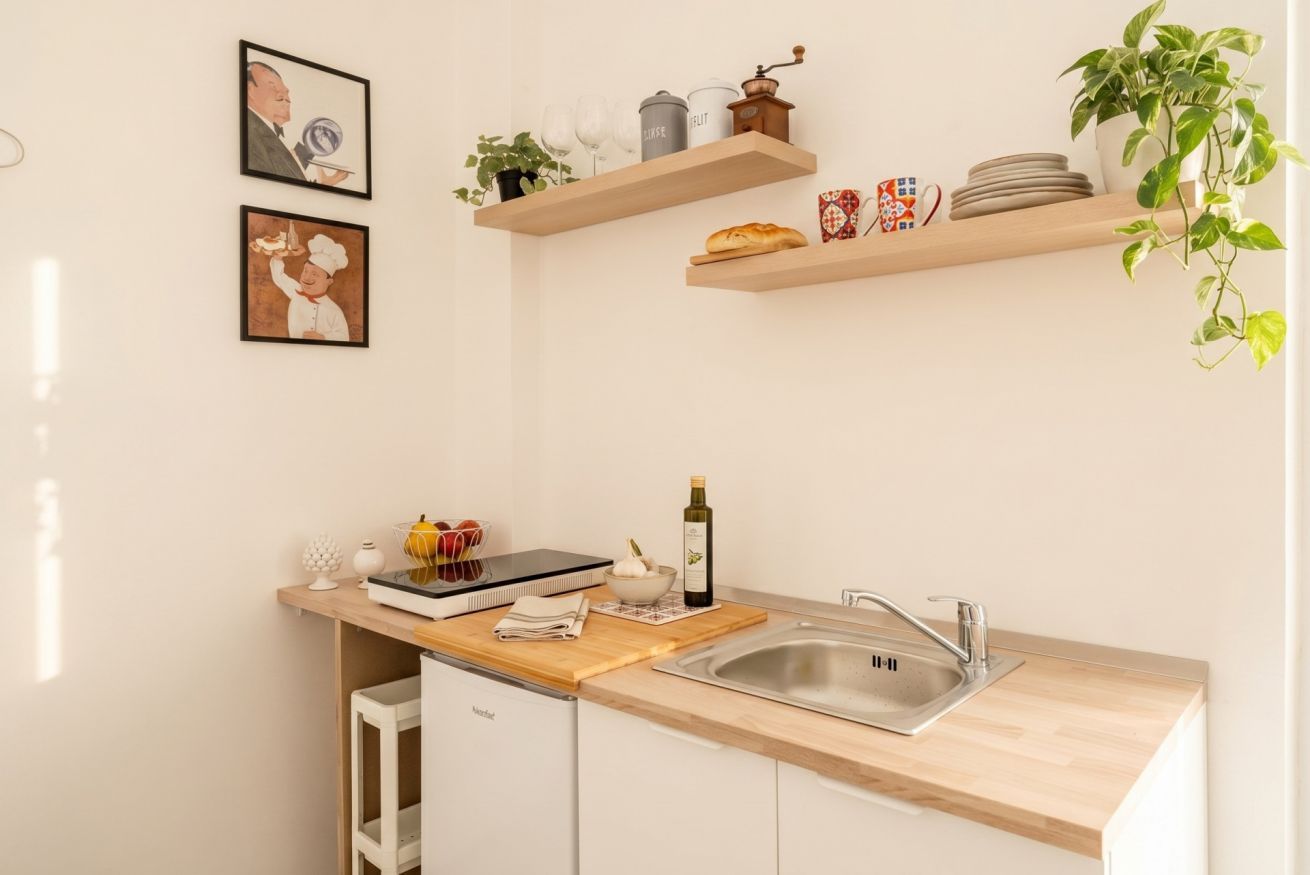 A kitchen with wooden shelves, a sink, and a compact refrigerator.