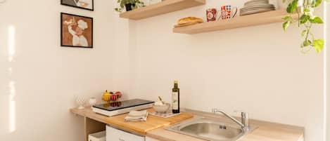 Una cocina con estantes de madera, un lavamanos y un refrigerador compacto.