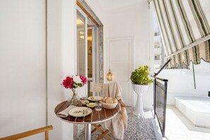 A dining area with a table set for two, a potted plant, and a view of the outside.