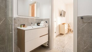 A modern bathroom with a glass shower enclosure, a white vanity with a mirror, and a tiled floor.
