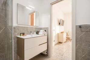 A modern bathroom with a glass shower enclosure, a white vanity with a mirror, and a tiled floor.