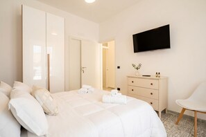 Quarto de hotel com cama, televisão, penteadeira e uma cadeira.