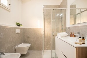 A modern bathroom with a glass shower enclosure, a white toilet, a sink with toiletries, and a mirror above the sink.