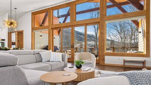 A spacious living room with a large sectional sofa, a round coffee table, and a view of a mountainous landscape through large windows.