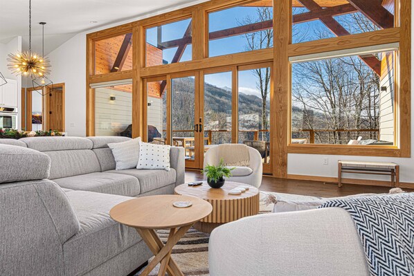 A spacious living room with a large sectional sofa, a round coffee table, and a view of a mountainous landscape through large windows.