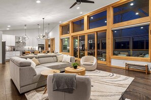 A modern living room with a sectional sofa, a round coffee table, and a large window with wooden frames.