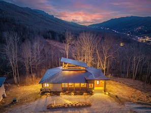 A modern house with a sloped roof, large windows, and a well-lit exterior.