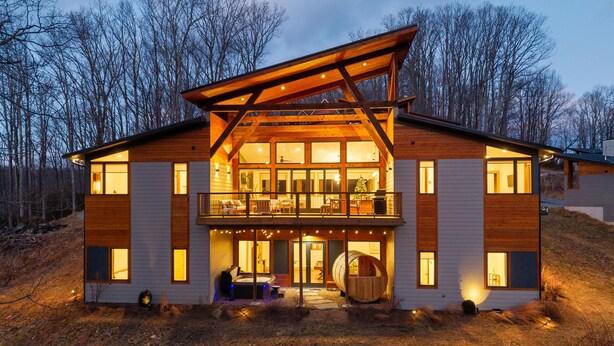 A modern log cabin with a large balcony, multiple windows, and a wooden exterior.