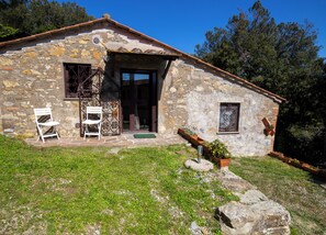 A stone building with a tiled roof, a wooden door, and a small window. There are two white chairs outside and a potted plant near the entrance. - Completely renovated, independent farmhouse. (Caldana)