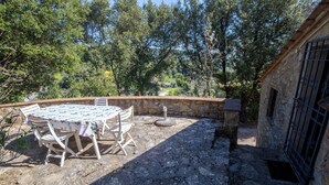 Un patio exterior con una mesa y sillas, rodeado de muros de piedra y árboles.