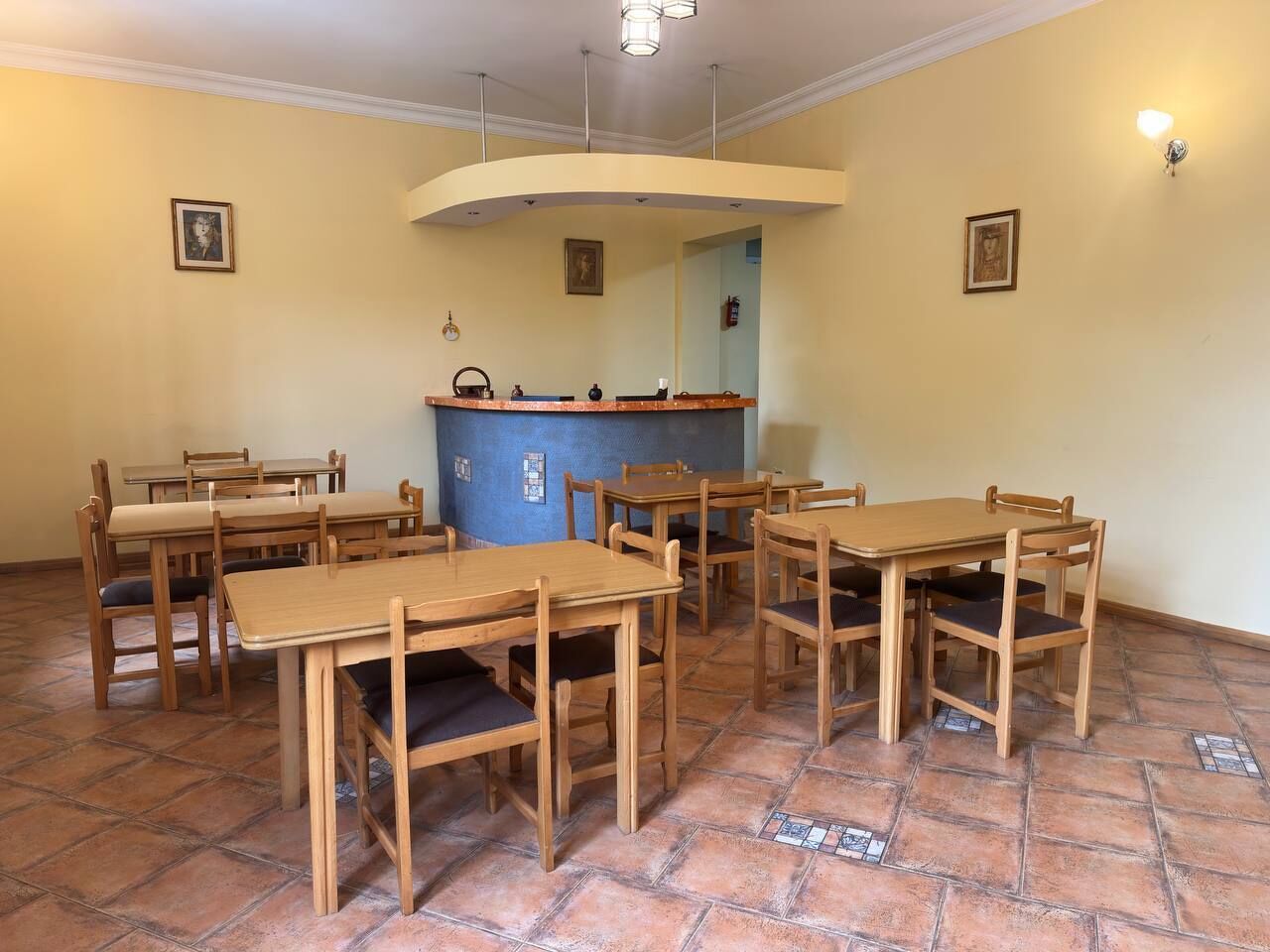 A dining area with wooden tables and chairs, a blue counter, and tiled flooring.