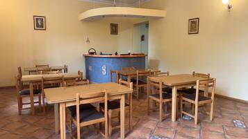 A dining area with wooden tables and chairs, a blue counter, and tiled flooring.