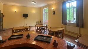 Un espace repas avec des tables et des chaises en bois, un téléviseur fixé au mur et une fenêtre avec des rideaux.