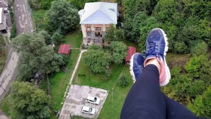 Une maison avec un toit bleu, entourée de verdure et dotée d’une allée pavée où sont garées deux voitures.