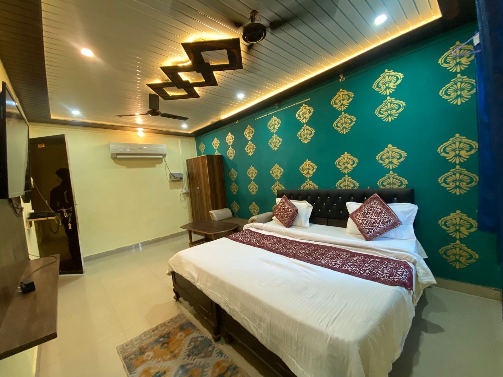 A hotel room with a bed, a wardrobe, a desk, and a patterned wall.