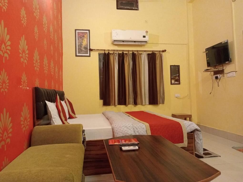 A hotel room with two beds, a sofa, a TV, and an air conditioner.