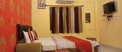 A hotel room with two beds, a sofa, a TV, and an air conditioner.