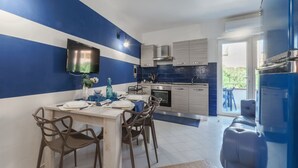 A modern kitchen with a blue and white color scheme, a dining area with a table and chairs, and a built-in TV on the wall. - BLUE MARINE: cozy apartment 200 meters from the sea (Ugento)