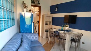 A modern living room with a blue sofa, a dining area with a table set for four, and a kitchen in the background. - BLUE MARINE: cozy apartment 200 meters from the sea (Ugento)