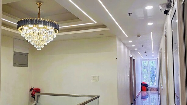 A modern hotel corridor with a glass railing, a chandelier, and a marble floor. - Hotel Urban Inn (Prayagraj)