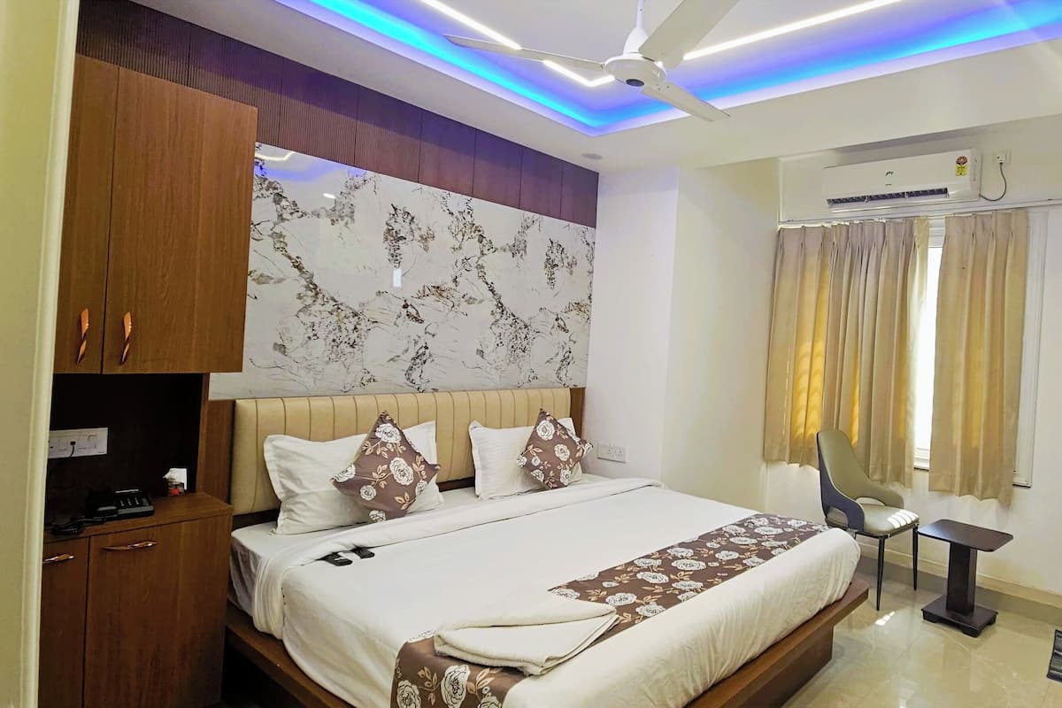 A hotel room with a bed, a desk, a chair, a TV, an air conditioning unit, and a ceiling fan.