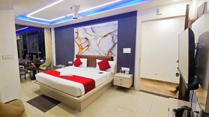 A modern bedroom with a large bed, bedside tables, a TV, and a mirror. - Hotel Urban Inn (Prayagraj)