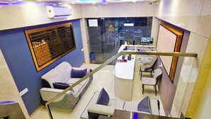 A hotel room with a blue accent wall, a white sofa, a small table, and a desk with chairs. - Hotel Urban Inn (Prayagraj)