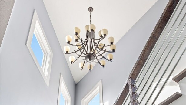 Una escalera de diseño moderno, con barandilla de metal y baranda de madera. Se observa un candelabro colgando del techo, y un perchero en la pared.