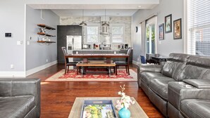 Una sala moderna con un sofá de cuero, una zona de comedor con mesa de madera, y una cocina al fondo.