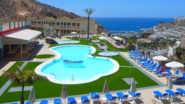 A resort with a large swimming pool, sun loungers, and a view of the ocean. - Natural Park (Mogán)