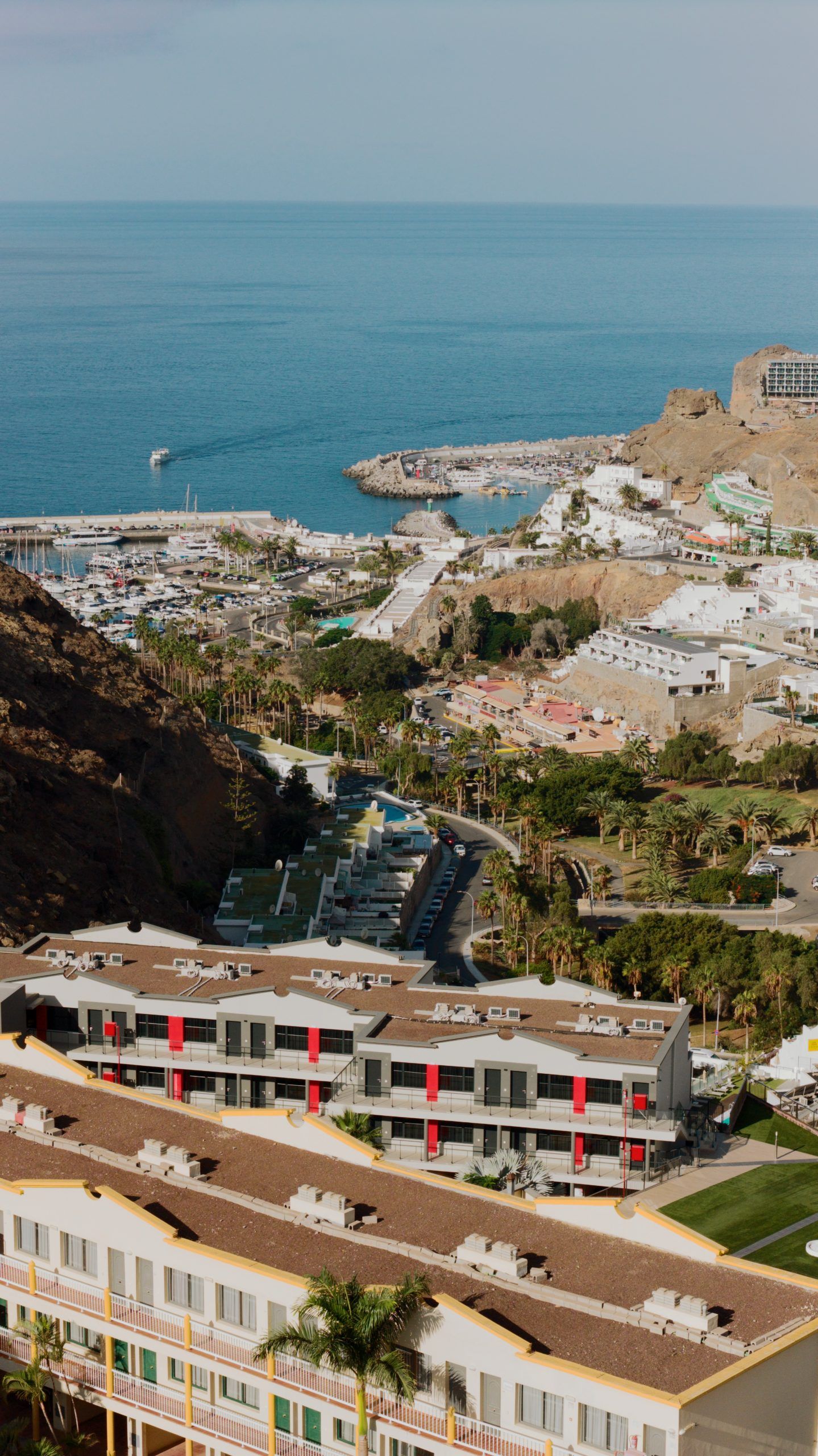 A coastal resort with a marina, buildings with balconies, and a view of the sea.
