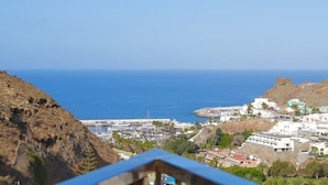 A coastal town with rocky terrain, a marina, and buildings with white and green facades. - Natural Park (Mogán)