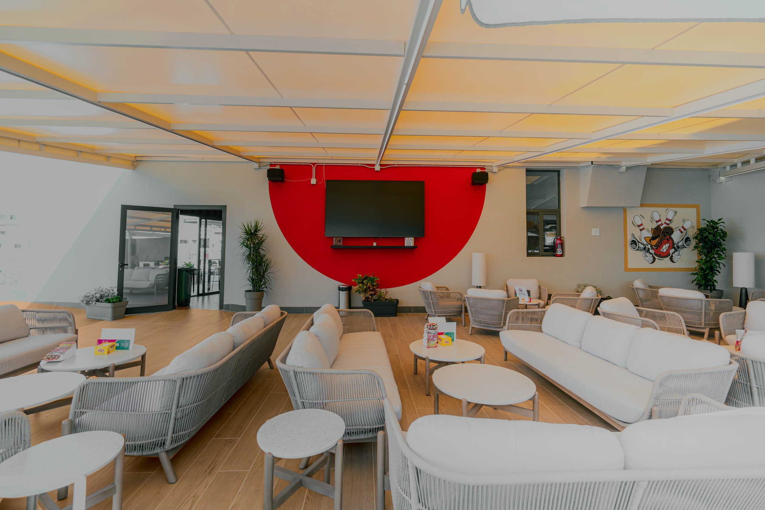 A modern lounge area with seating arrangements, a large screen, and a red accent wall.