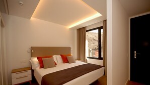 A modern hotel room with a large bed, a bedside table, and a window with a view of a mountainous landscape. - Natural Park (Mogán)