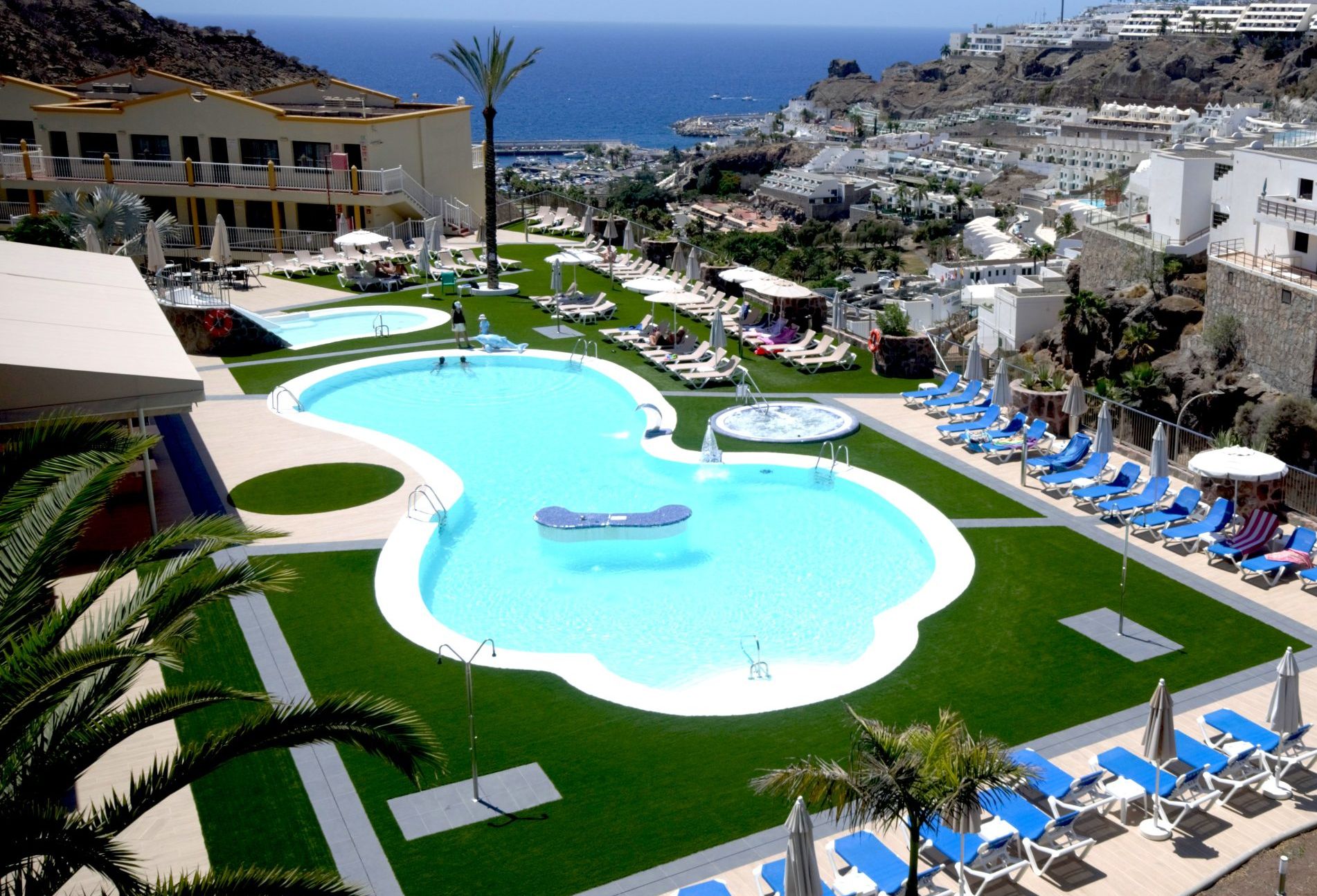Un resort con una piscina grande, tumbonas y vista al océano.