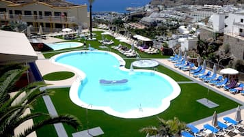Un resort con una piscina grande, tumbonas y vista al océano.