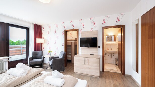 Ein Hotelzimmer mit zwei Betten, einem Fernseher, einem Schreibtisch, einem Stuhl, einem Kleiderschrank und einem Badezimmer.
