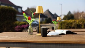Ein Holztisch mit einer klaren Glasvase, in der rote Tulpen stehen, einer schwarzen Tasse und einer gelben Lampe.