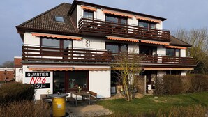 Ein zweistöckiges Haus mit Balkon und Eingang. Ein Schild weist auf einen Betrieb im Erdgeschoss hin.