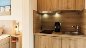 Et lille køkken med træskabe, en indbygget komfur, en kaffemaskine og en vask.