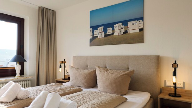 Et hotelværelse med to senge, et maleri af en strand og udsigt til havet.