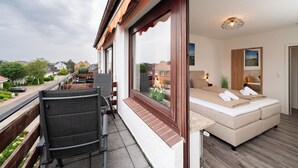 A balcony with a sofa and chairs, a wooden floor, and a view of neighboring houses. - Quartier 16<br>Apartment in a quiet location and access to sea time (Büsum)