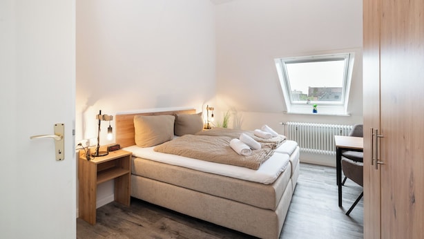 A bedroom with a bed, bedside table, lamp, and a window with a view.