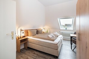 A bedroom with a bed, bedside table, lamp, and a window with a view. - Quartier 17<br>Apartment in a quiet location and access to sea time (Büsum)