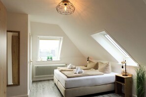 Ein Schlafzimmer mit schrägem Dach, Oberlicht, Heizkörper, einem Bett mit Handtüchern und einem Nachttisch mit Lampe.