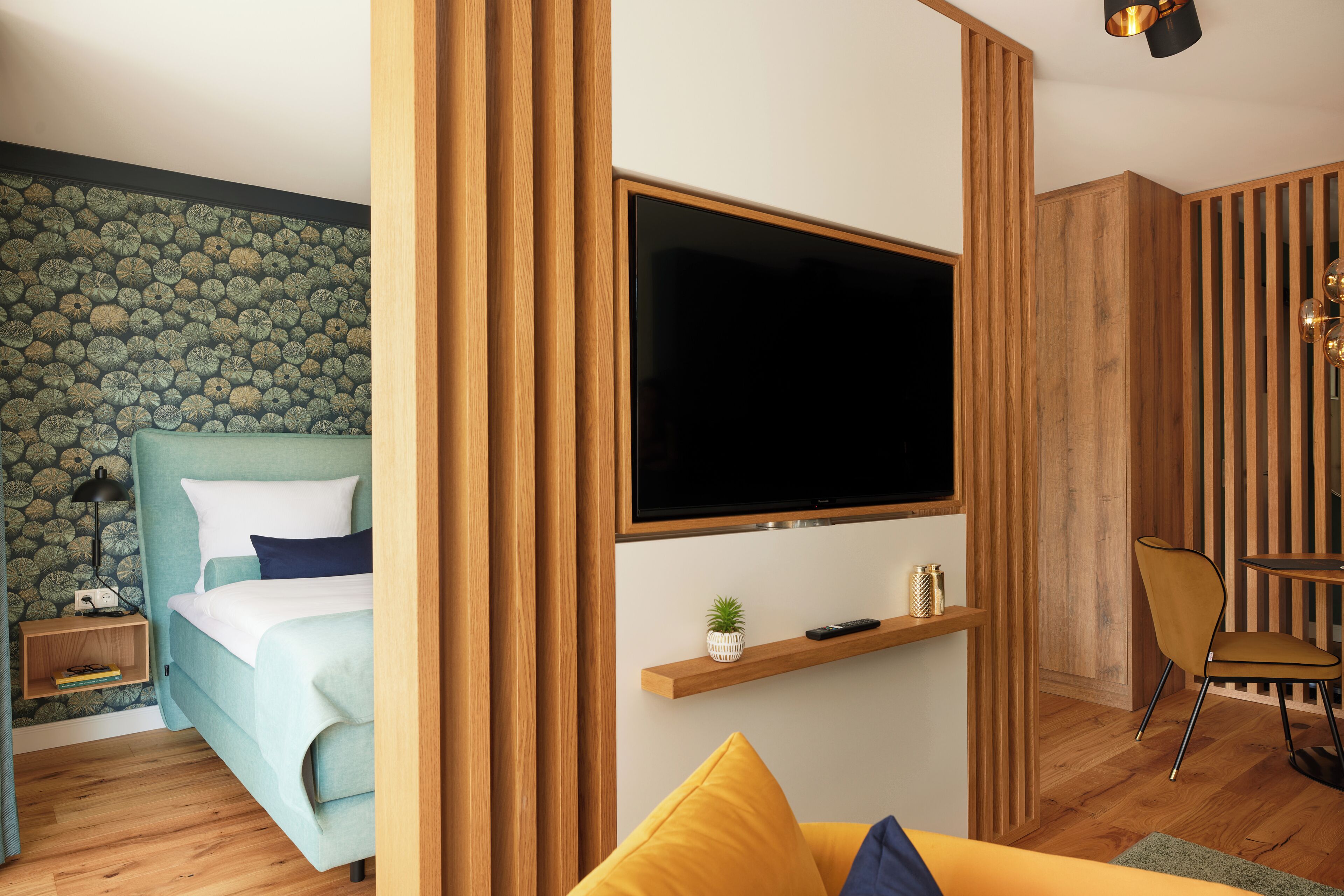 Un dormitorio moderno con una cama, un televisor en la pared, una mesita de noche y un pequeño estante con adornos.