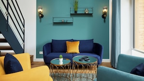 A modern living room with a teal accent wall, a blue sofa, yellow and blue armchairs, and two round tables with decorative items. - Completion 2025: Exclusive accommodation with balcony close to the beach! (Sankt Peter-Ording)
