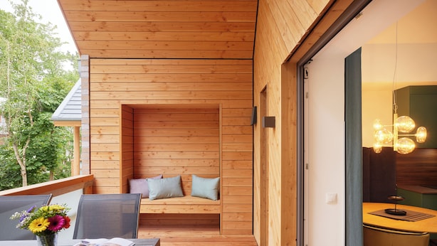 A wooden deck with a bench, a table with a vase of flowers, and a dining area with chairs and a lamp. - Completion 2025: Exclusive accommodation with balcony close to the beach! (Sankt Peter-Ording)