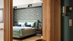 A modern bedroom with a green bed, wooden floor, and a patterned wallpaper.